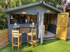 an outdoor bar with wooden chairs and tables in the grass next to a small shed