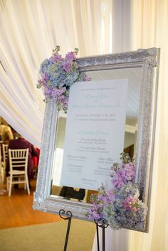 a wedding program is displayed in front of a mirror with purple and blue flowers on it