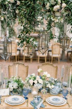 the table is set with blue and white plates, silverware, flowers and greenery