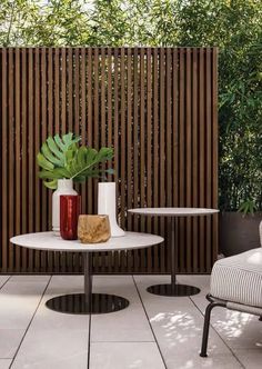 two chairs and a table in front of a wooden privacy wall with plants on it