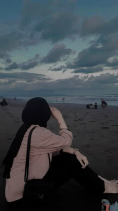 a woman sitting on top of a beach next to the ocean under a cloudy sky