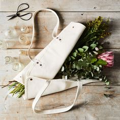 a bouquet of flowers and scissors on a wooden table next to an old canvas bag