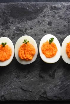 four deviled eggs with carrots in them sitting on a black slate counter top