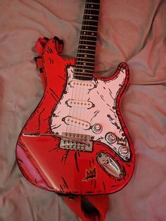 an electric guitar is laying on a pink sheet with red and white designs painted on it