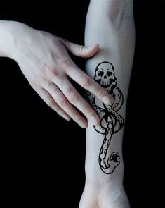 a person with a skull and snake tattoo on their left arm, holding onto another hand