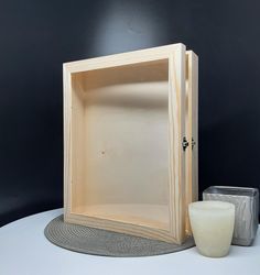 an empty wooden box sitting on top of a table next to a vase and candle