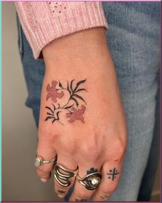 a woman's hand with tattoos and rings on her left wrist, showing the flower tattoo