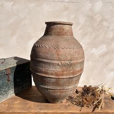 an old vase sitting on top of a wooden table next to a box and plant