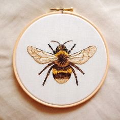 a close up of a bee on a piece of cloth in a hoop with embroidery