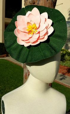 a white mannequin head with a pink flower on it's top and green leaves