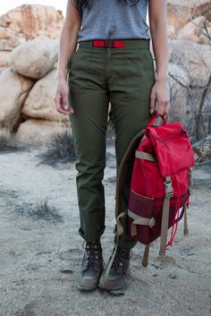 a woman standing in the desert with a backpack on her back and one handbag hanging from her shoulder