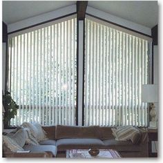 a living room with couches and large window covered in white vertical blind blinds on the windows