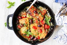 a skillet filled with chicken, rice and olives on top of a wooden table