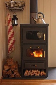 a wood burning stove with logs stacked on the floor next to it and a tea pot hanging above