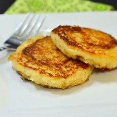 two pancakes sitting on top of a white plate with a fork and knife next to it