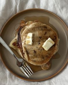 a plate topped with pancakes covered in butter and syrup next to a knife and fork