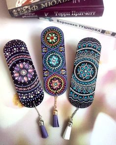 three bookmarks with beads and tassels are on a table next to some books