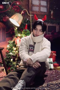 a man sitting in front of a christmas tree wearing a scarf and reindeer antlers on his head