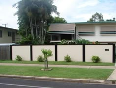 a white house with green plants on the side of it and a black fence in front