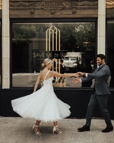 a bride and groom dancing on the sidewalk in front of a storefront with an art deco sign