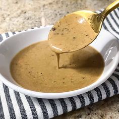 a white bowl filled with sauce and a golden spoon in it on top of a black and white towel