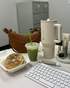 a table topped with a cup of coffee and a bagel next to a keyboard