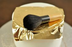 a close up of a brush in a gold foil container on a white cake plate