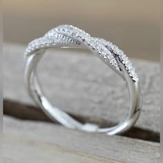 a white gold wedding ring with diamonds on the top and bottom, sitting on a piece of wood