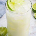 a glass filled with limeade next to sliced limes on a white tablecloth