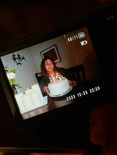 a woman holding a cake with lit candles on it in front of her phone screen