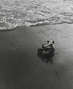 black and white photograph of a motorcycle on the beach with waves coming in to shore