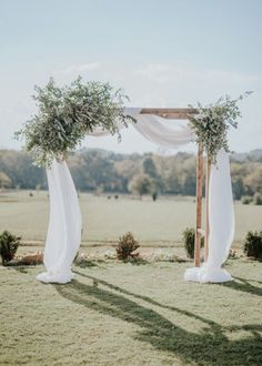 an outdoor ceremony setup with white drapes and greenery