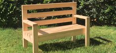 a wooden bench sitting on top of a green grass covered park field next to bushes