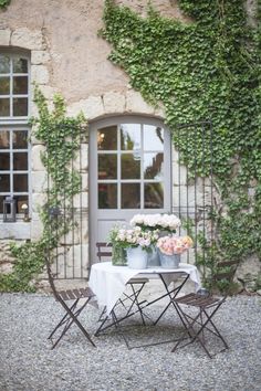 a table and chairs with flowers on them in front of a building that has ivy growing over it