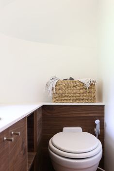 a white toilet sitting inside of a bathroom next to a wooden cabinet and counter top