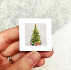 a hand holding a small card with a christmas tree on it