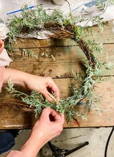 someone is making a wreath out of branches and flowers on a table with other items