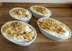 four white bowls filled with food on top of a wooden table