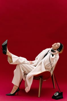 a woman laying on top of a red chair next to a black phone and telephone