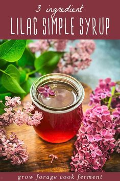 a jar filled with liquid sitting on top of a wooden table next to purple flowers