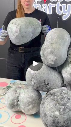 a woman standing next to a pile of gray balls on top of a white table