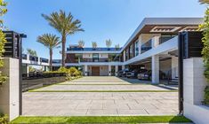 the entrance to a modern home with palm trees in the back ground and cars parked on the driveway