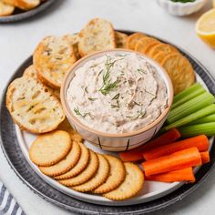 a plate with crackers, carrots and dip on it