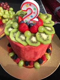 a birthday cake made to look like fruit with the number 2 on top and two candles in the middle