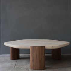 an oval table with two wooden bases on the floor in front of a gray wall