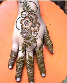 the hand is decorated with henna and flowers on it's palm, which has been placed on an orange surface