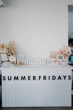 a white counter with flowers and candles on it that says summer fridays in black lettering