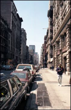 a man is walking down the sidewalk in front of parked cars and buildings on a sunny day