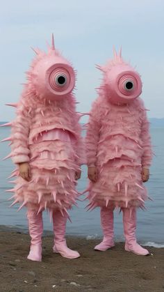 two people in pink furry costumes standing on the beach with their eyes wide open,