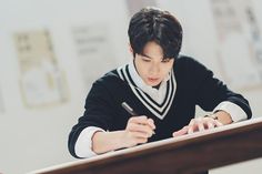 a young man sitting at a desk writing on a piece of paper with a pen in his hand